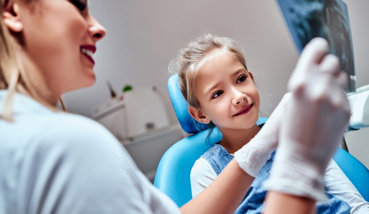 Dental team member talking to young girl in dental chair