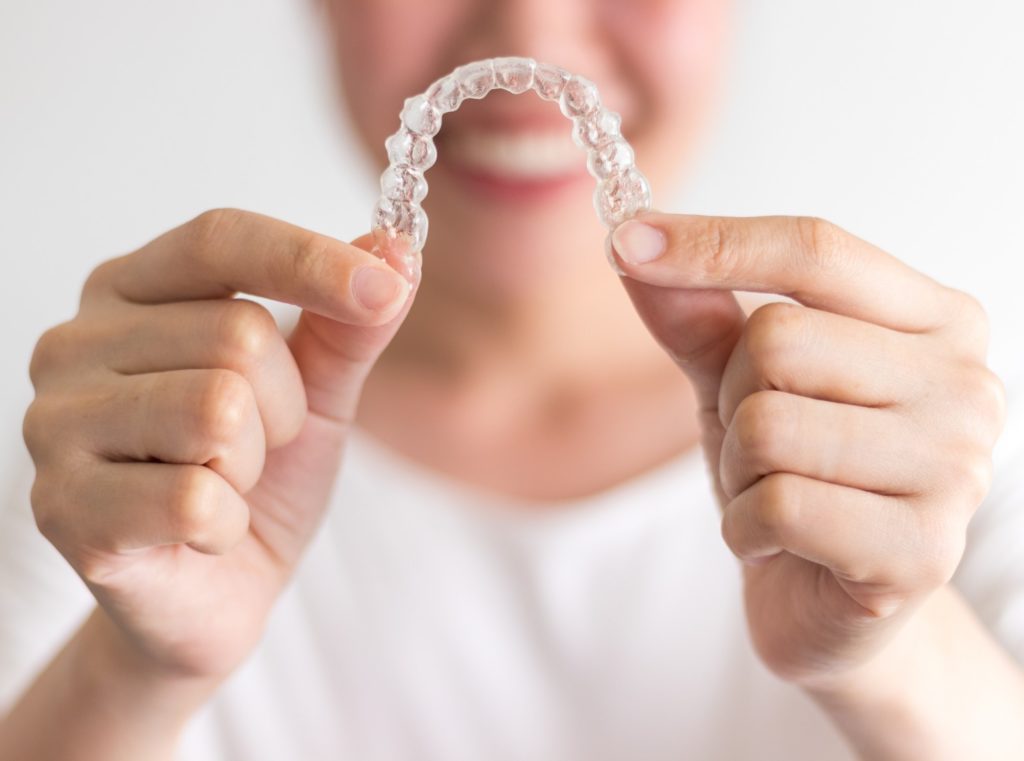 Woman in white shirt smiling while holding clear aligner